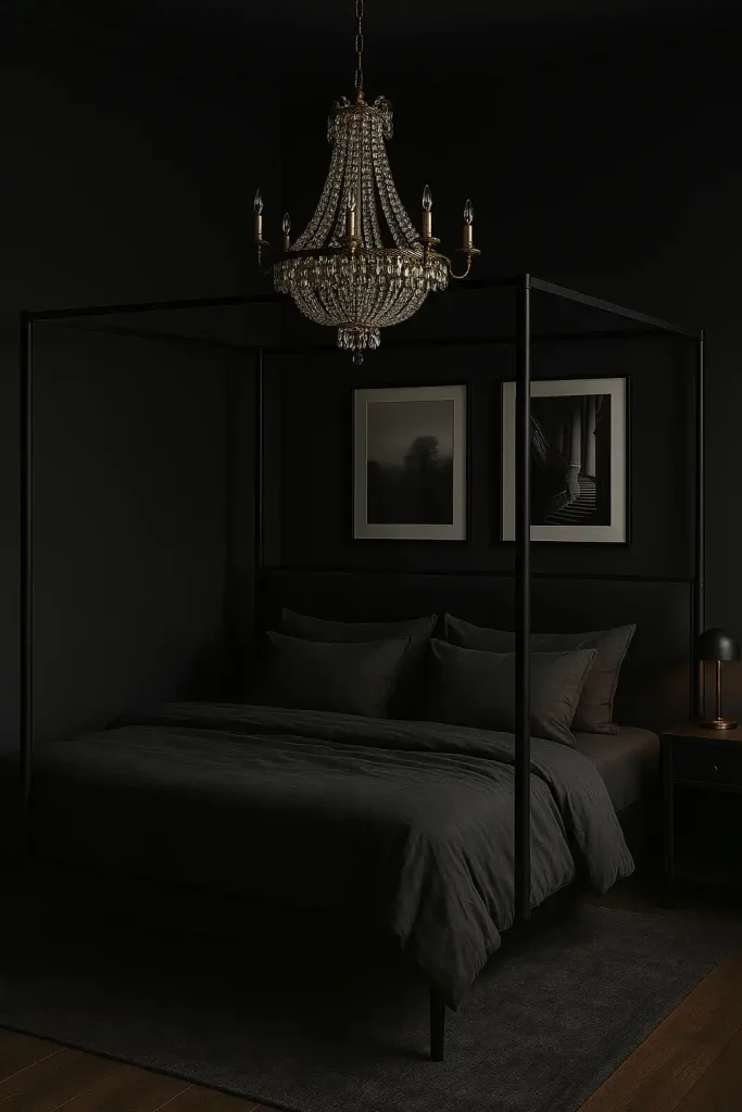 A luxurious black master bedroom with matte charcoal walls, black-and-white photography in thin black frames, and a four-poster bed with dark gray bedding. A crystal chandelier adds contrast and glam.
